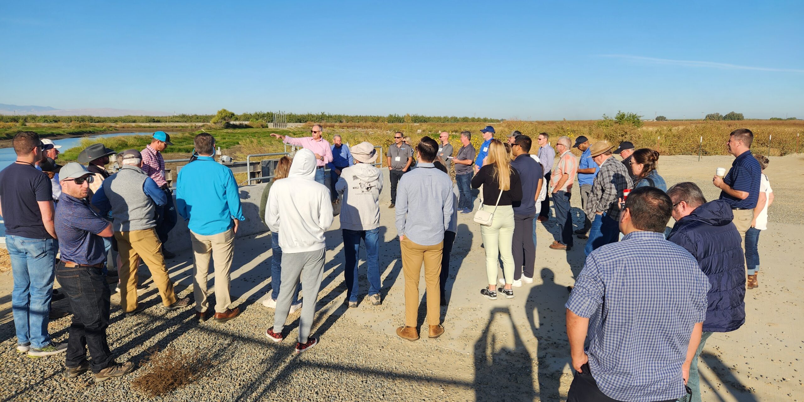 People standing near a canal and large pump listening to a presentation about how the recharge and flood control project was constructed and funded.