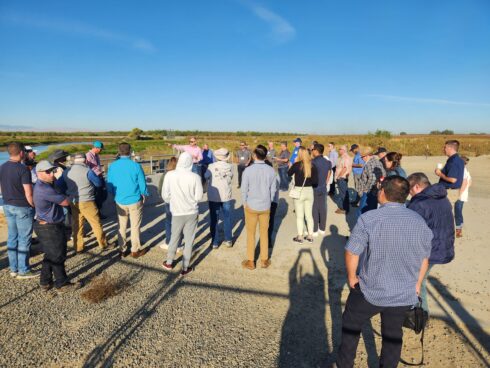 People standing near a canal and large pump listening to a presentation about how the recharge and flood control project was constructed and funded.