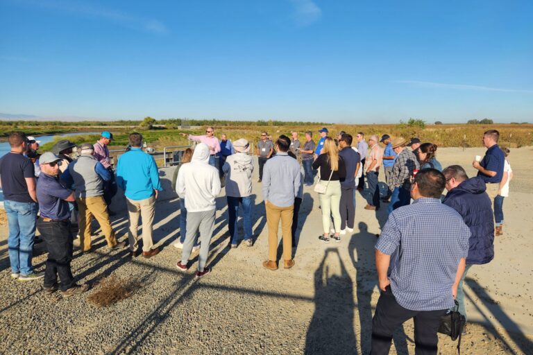 People standing near a canal and large pump listening to a presentation about how the recharge and flood control project was constructed and funded.